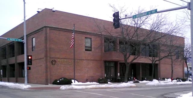 Brick courthouse building with an American flag and street signs for Pattee Street and Broadway Street.