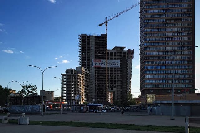 A construction crane stands between two multi-story buildings under construction in Moscow.