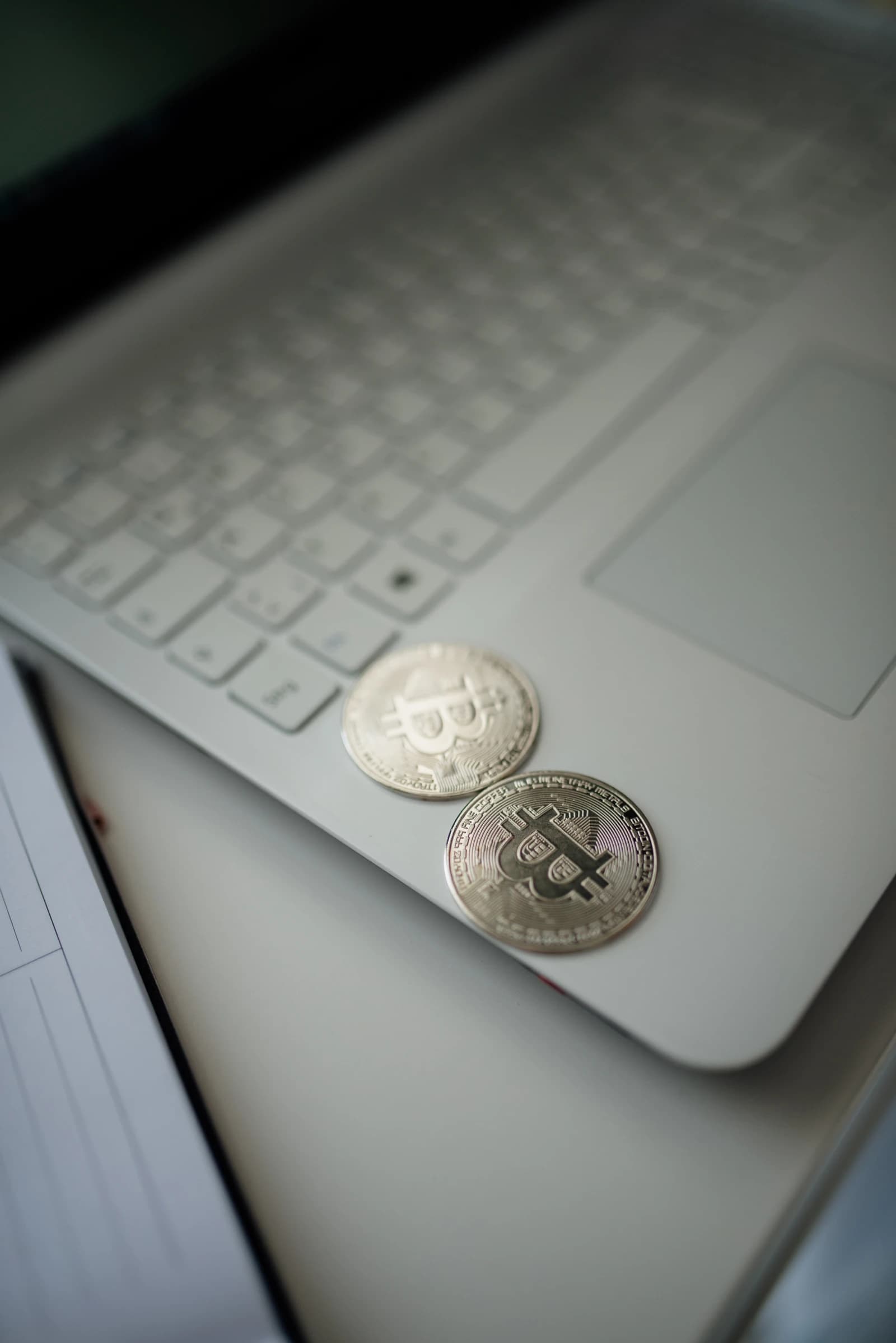 Two silver Bitcoin coins rest on a light-colored laptop keyboard.