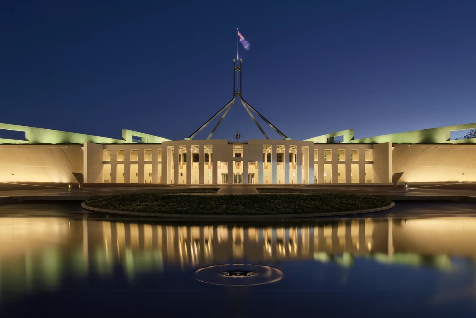 Parliament House in Canberra, Australia, illuminated at dusk with reflections in a foreground pool.