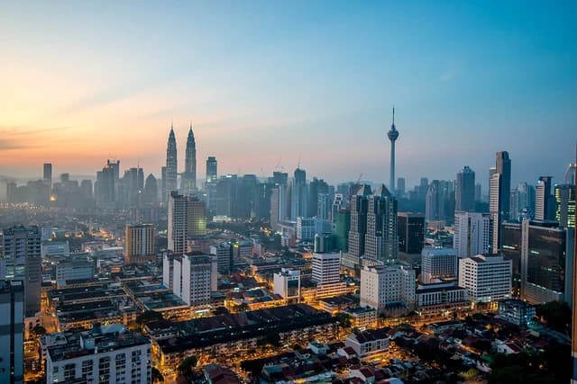Kuala Lumpur skyline at dawn with multiple high-rise buildings and a clear sky.