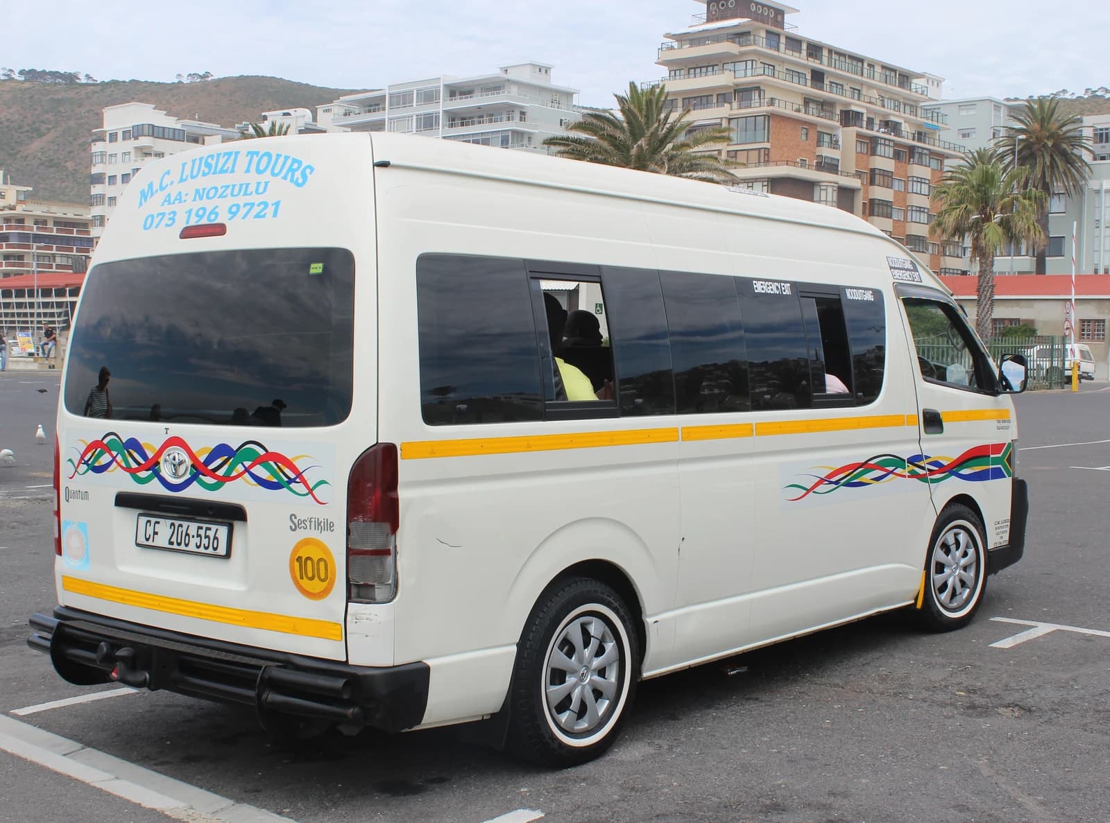 White South African minibus taxi, adorned with national flag colors, parked on asphalt.