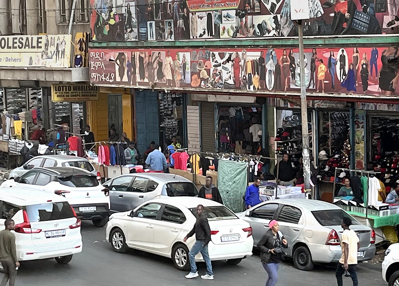 People walking past street vendors and cars on a busy street.