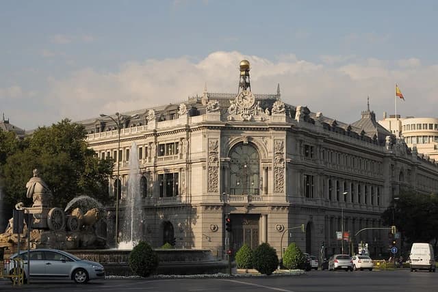 Bank of Spain building in Madrid, a large ornate stone structure, with a fountain nearby.