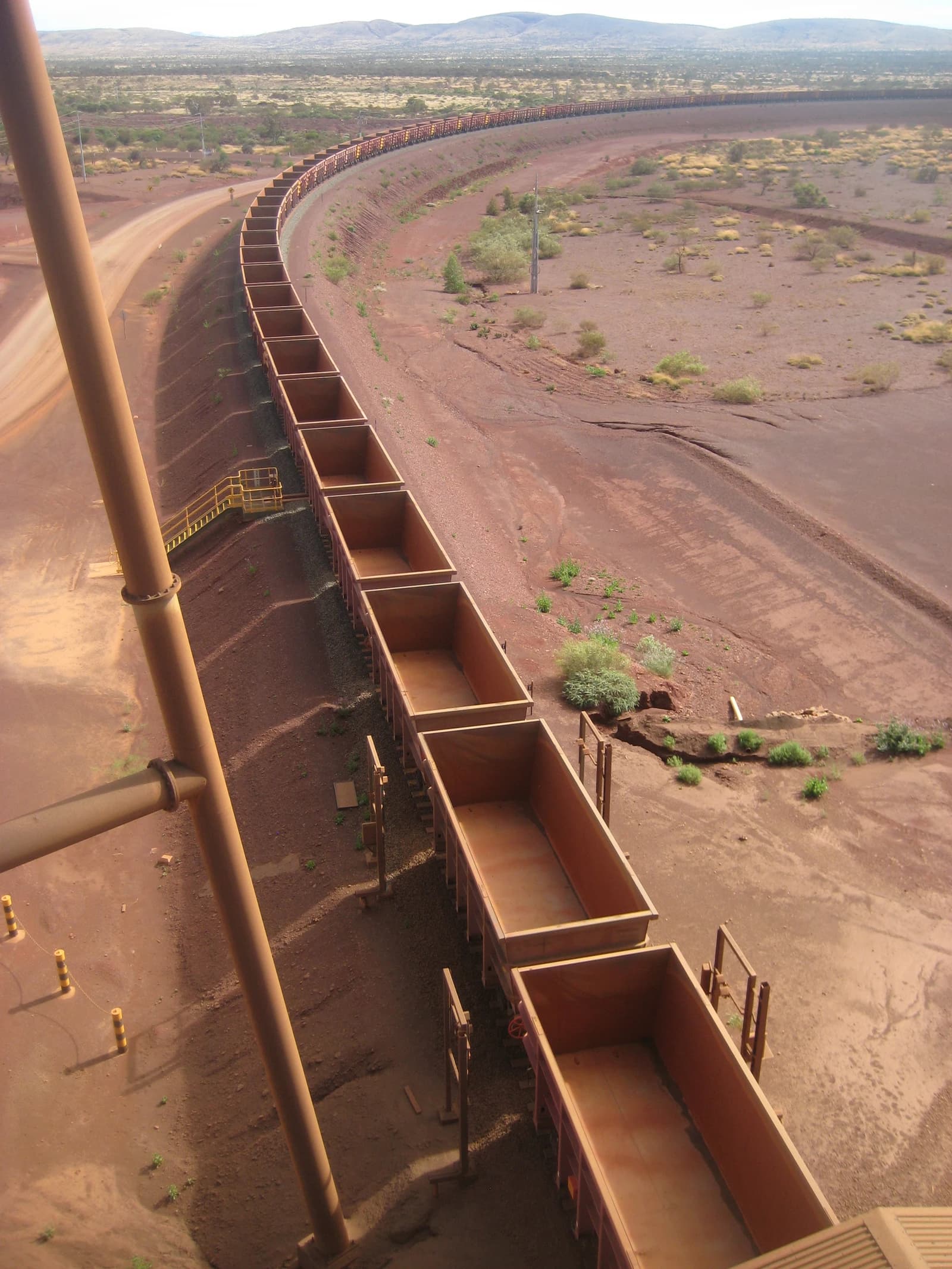 An iron-ore train, with numerous empty wagons, curves through a reddish, arid landscape.
