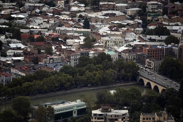 Aerial view of residential buildings, a river, and a bridge in Tbilisi, Georgia.