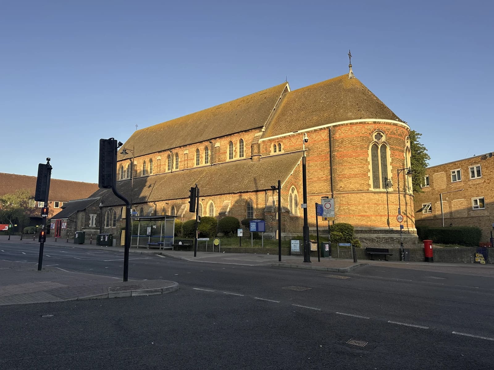 Brick church building with arched windows and a tiled roof at a street corner.