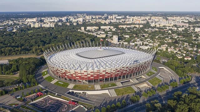 Aerial view of National Stadium Warsaw with city buildings and green areas in background.