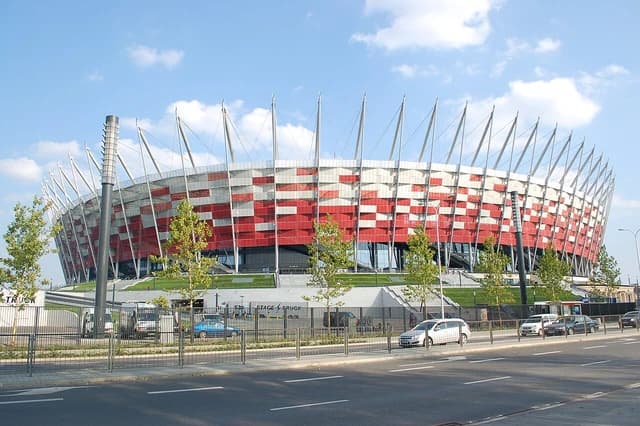 National Stadium in Warsaw, Poland, with red and white facade and supporting masts.