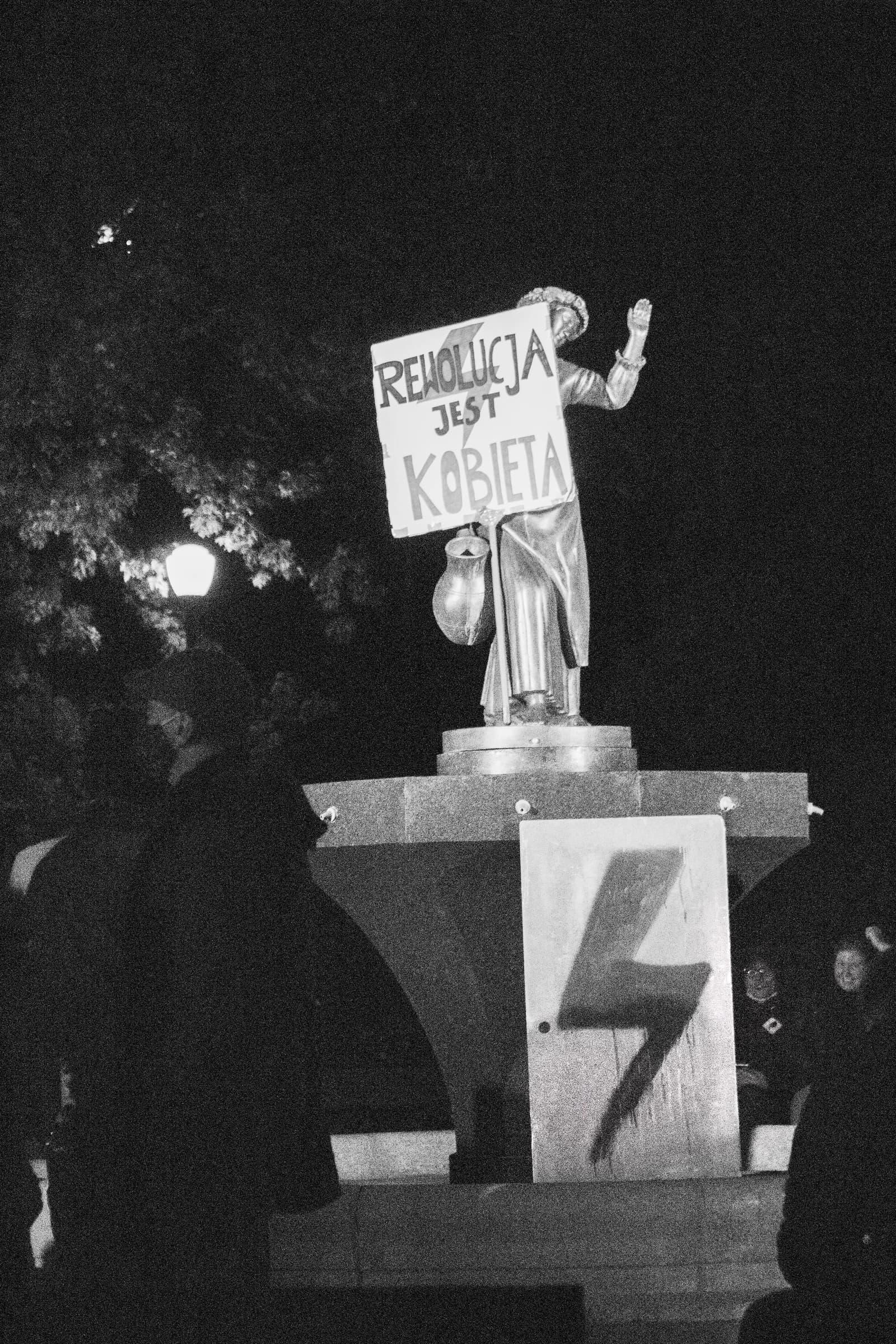 Statue holding a sign during a protest in Warsaw, Poland at night.
