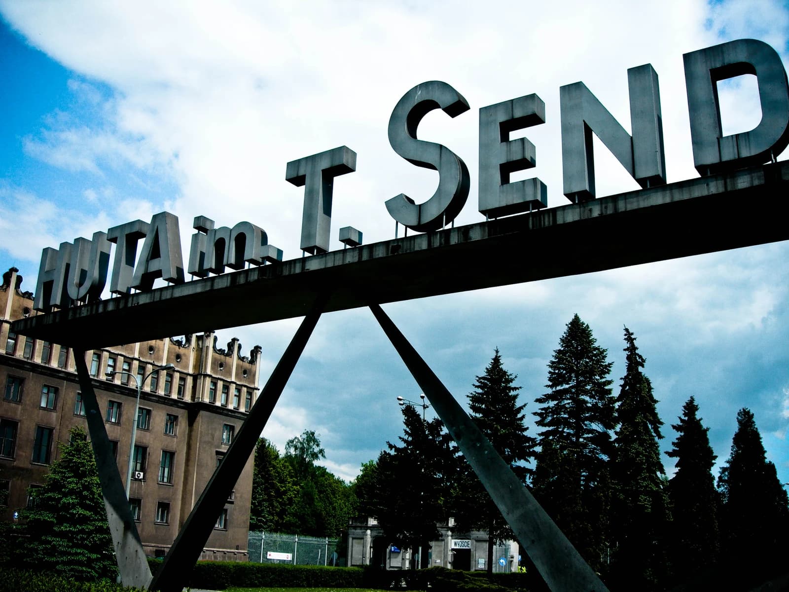 Sign for Huta im T. Sendzimira steelworks in Poland under a cloudy sky.