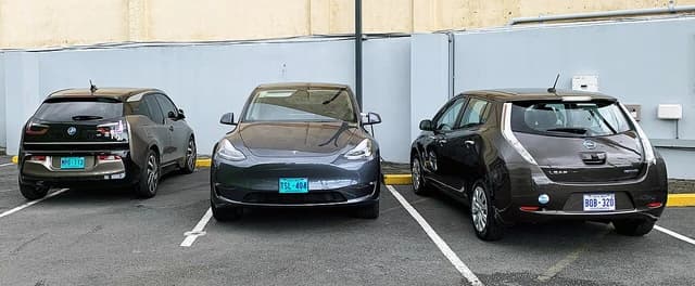 Three electric cars, including a gray Tesla, parked in a paved lot.