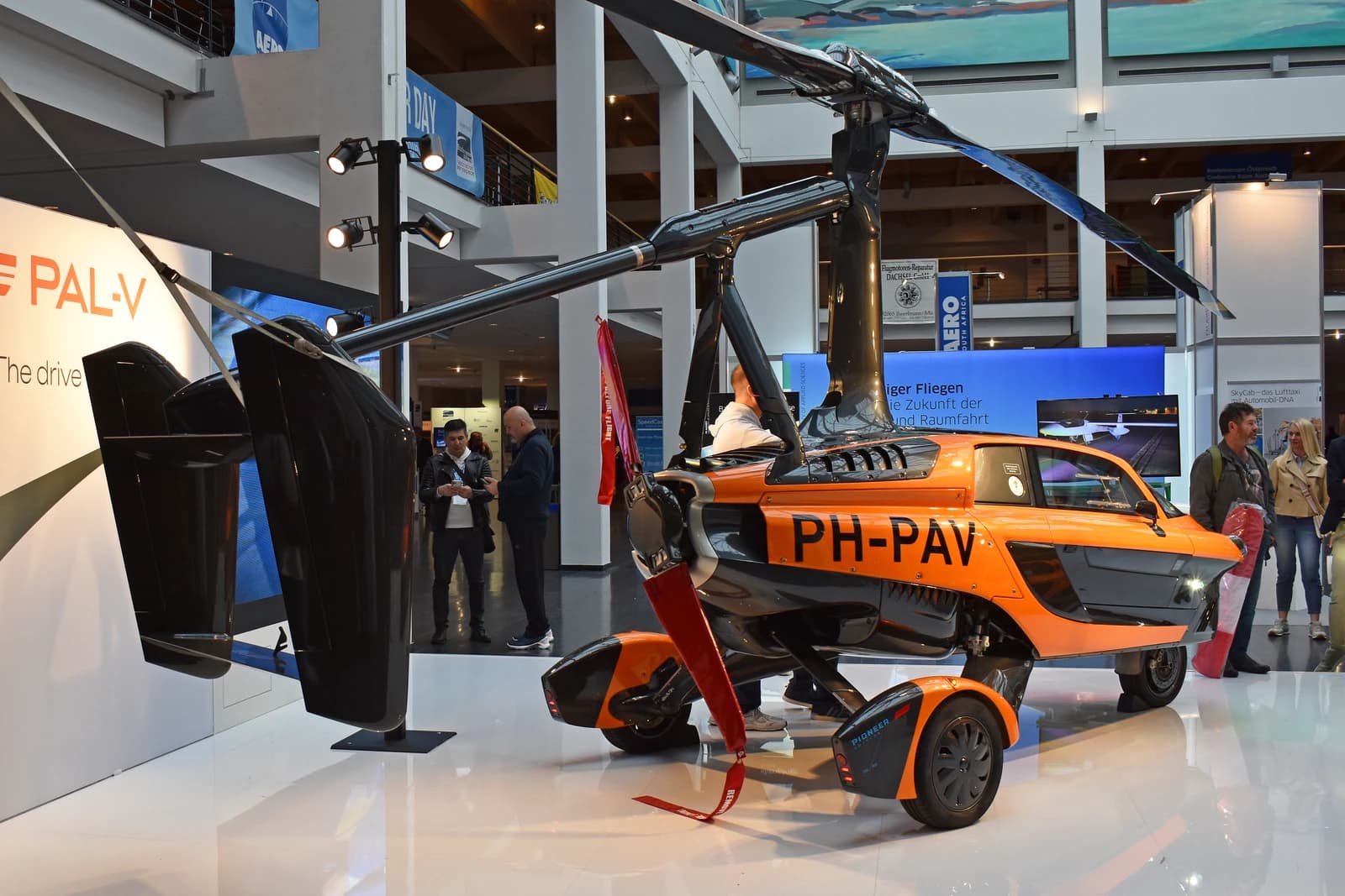 Orange and black PAL-V Liberty gyrocopter car with rotor blades deployed on display.