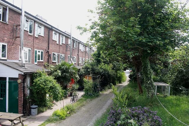 A residential street view of brick houses with green doors and gardens.
