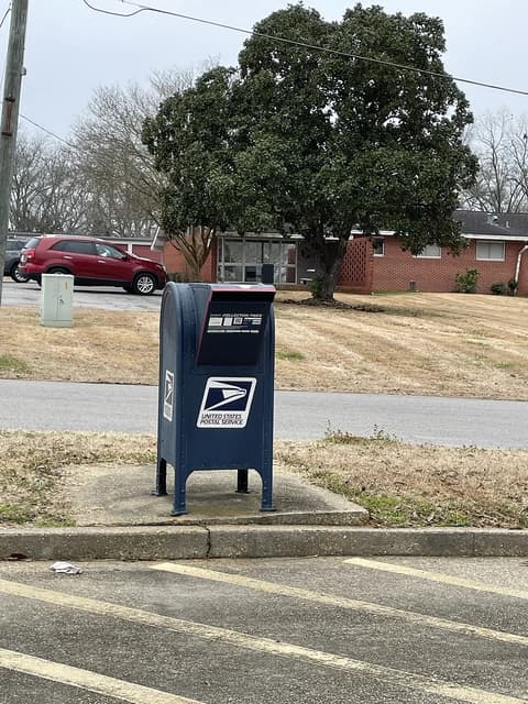 Blue USPS mail collection box with a residential background.