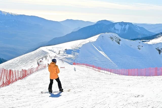 Young snowboarder standing on a ski slope overlooking snow-covered mountains.