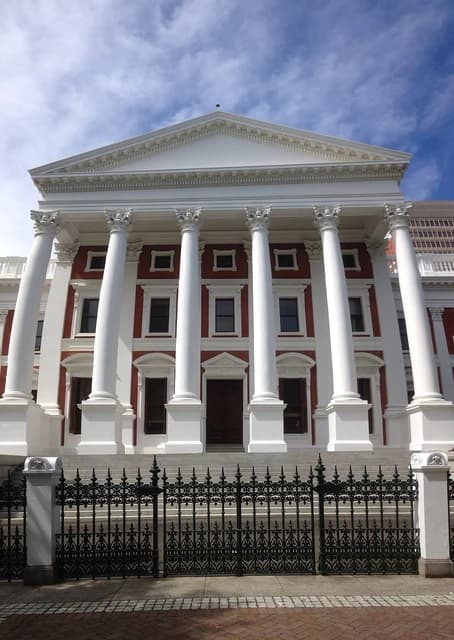 Grand facade of Houses of Parliament, Cape Town, with white columns and red walls.