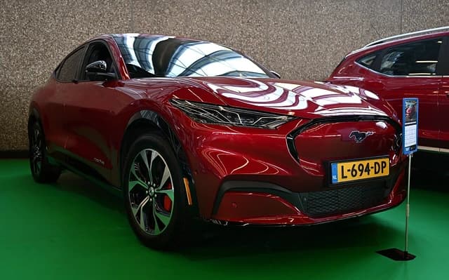 Red Ford Mustang Mach-E electric SUV displayed indoors, angled front-right view.