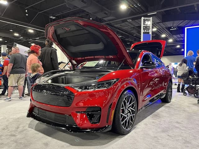 Red 2023 Ford Mustang Mach-E with hood open at an auto show.