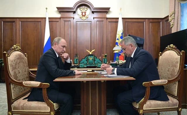 Russian President Vladimir Putin and Defense Minister Sergey Shoigu seated at a desk.