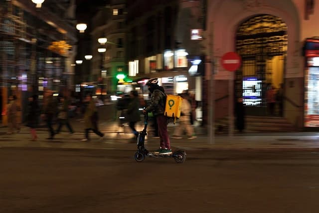 A Glovo rider operates a scooter on a city street at night in Madrid.