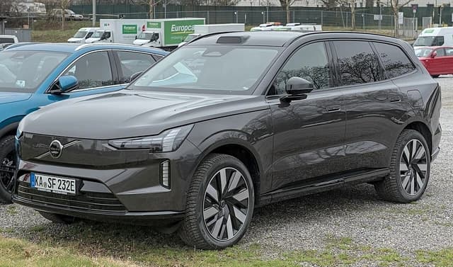A dark gray Volvo EX90 electric SUV parked on a gravel lot.