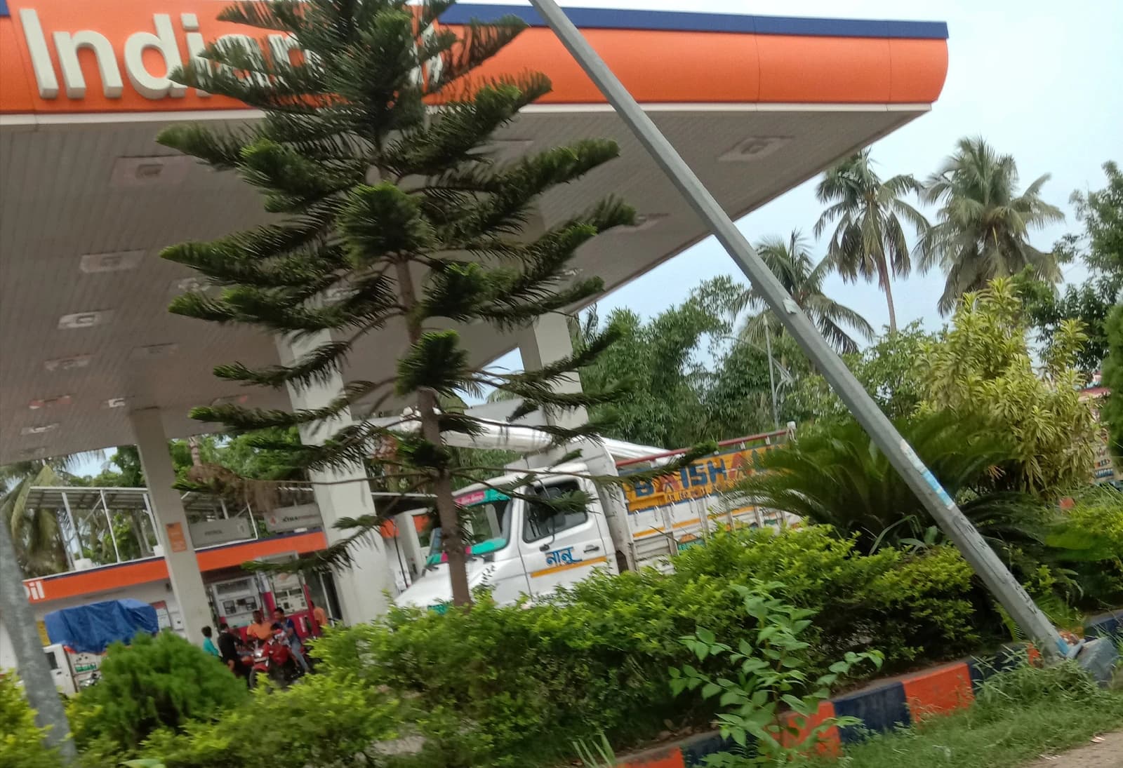 Indian Oil petrol pump with canopy, trees, and a truck partially visible.