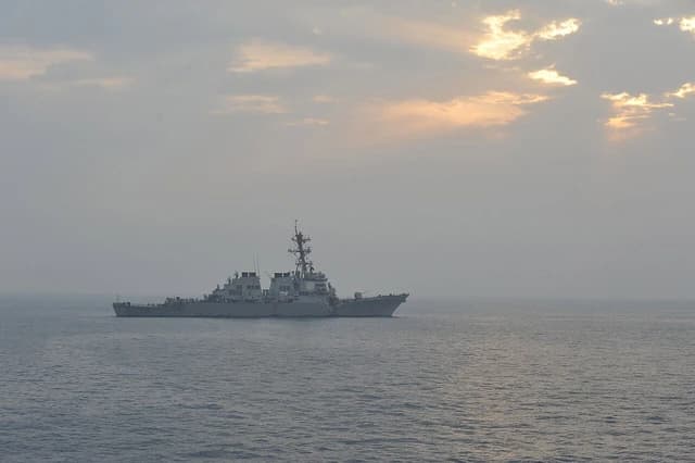 USS Porter, an Arleigh Burke-class destroyer, sailing in the ocean at sunrise or sunset.