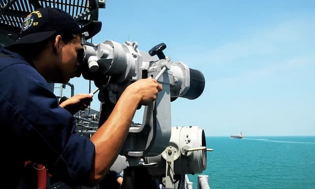 Seaman Anthony Brown observes boat traffic using ship-mounted binoculars aboard the USS Lake Champlain.