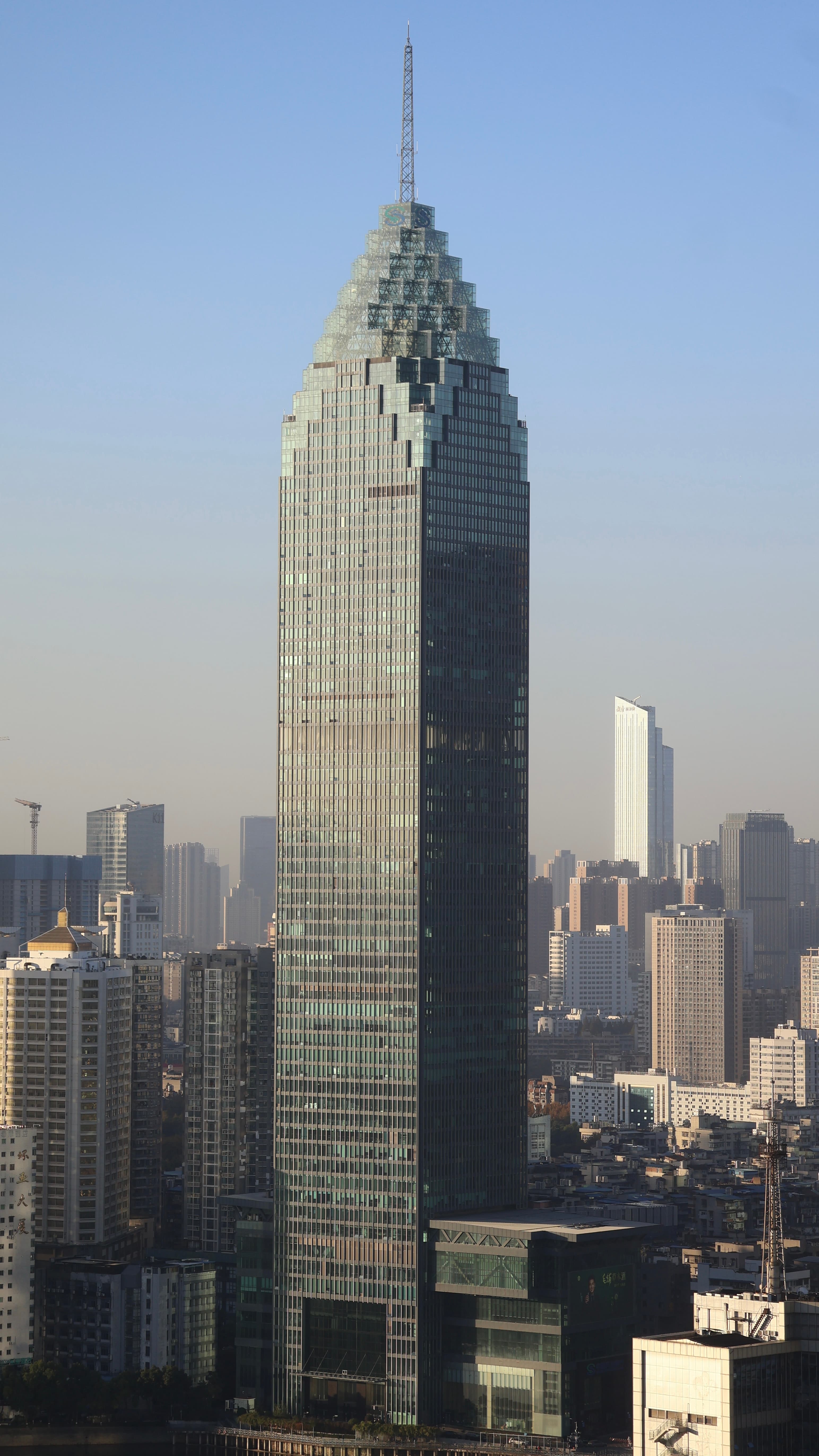 Skyscraper with a triangular, stepped roof and antenna against a hazy sky in Wuhan.