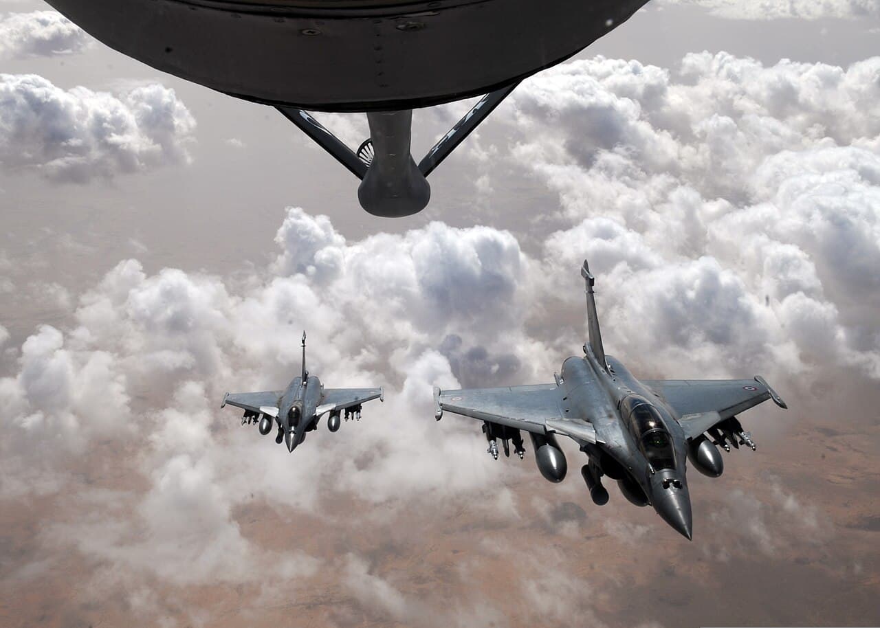 Two French Air Force Rafale fighter aircraft fly near a refueling aircraft.