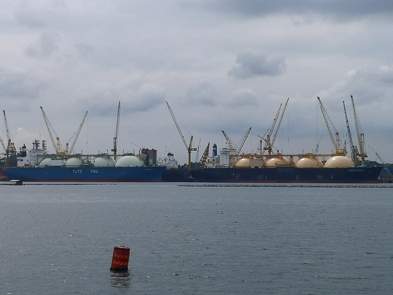 Two large liquefied natural gas carriers docked at a port with cranes visible in the background.