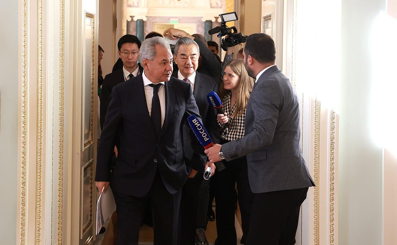Chinese Foreign Minister Wang Yi walking with an official and being approached by reporters.