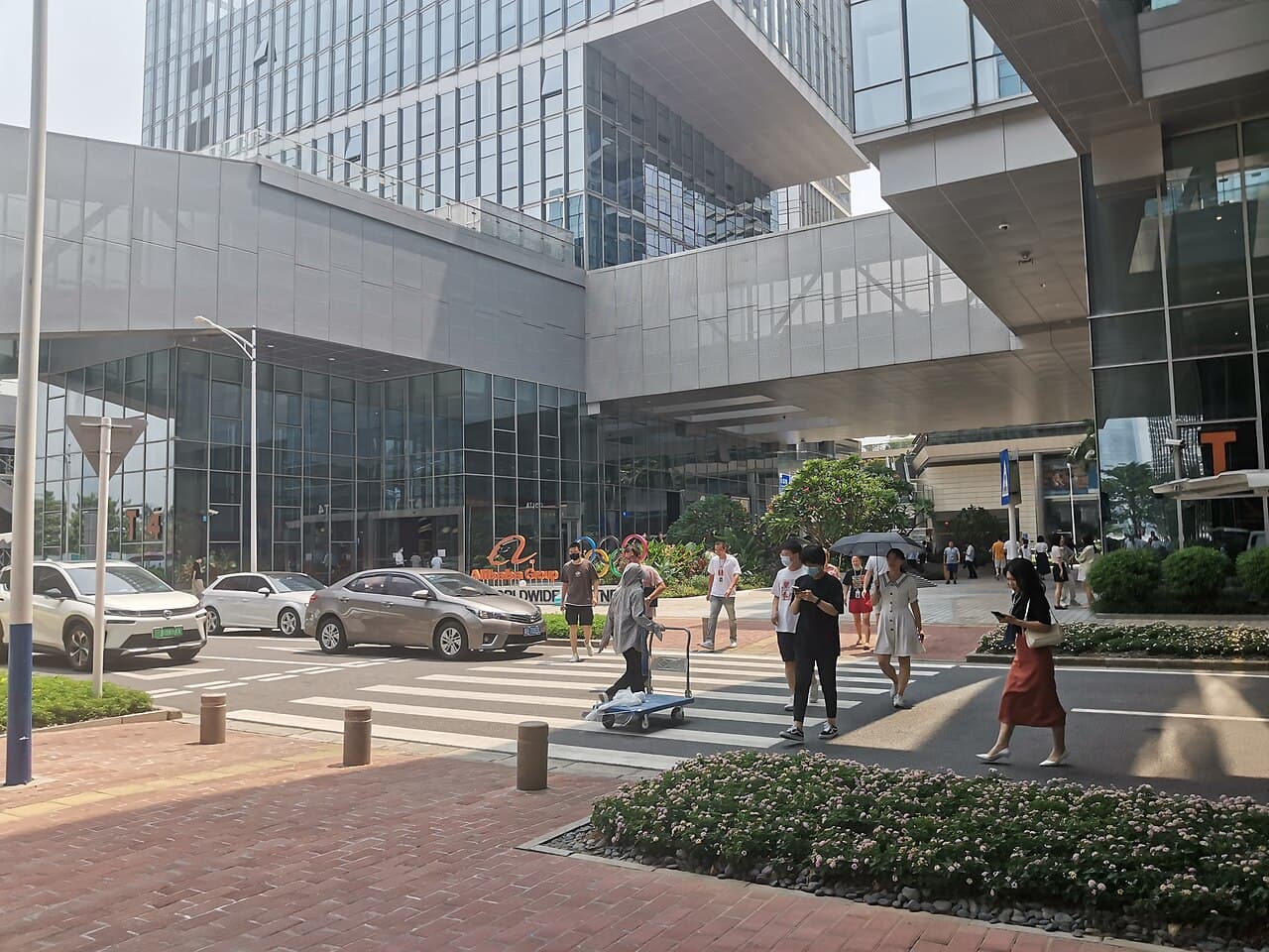 Pedestrians walk on a crosswalk in front of the modern Alibaba Shenzhen Branch building.